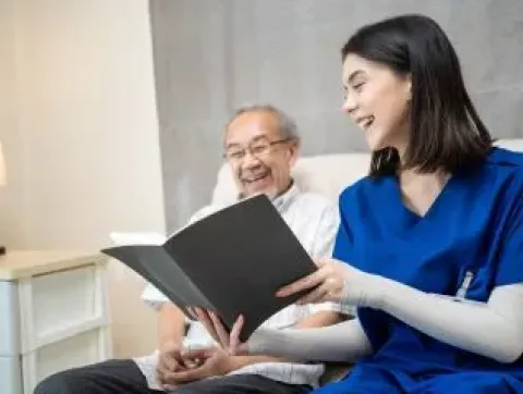 Doctor sharing a book with older Asian man in a hospital bed