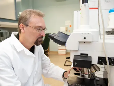 Dr. Larry Sanford studies a slide under a microscope.