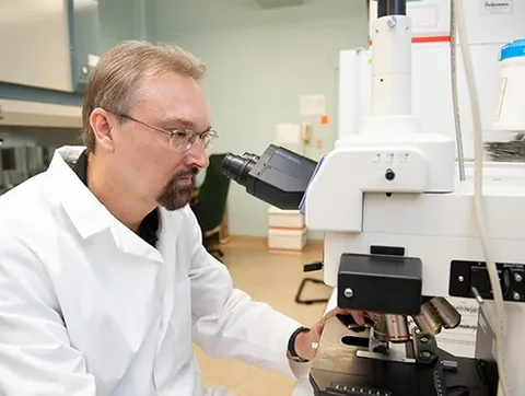 Dr. Larry Sanford studies a slide under a microscope.