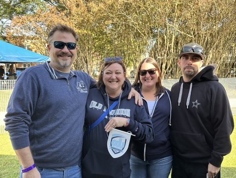 Four Old Dominion University alumni pose outdoors at an alumni event, smiling and wearing ODU-branded apparel and accessories.