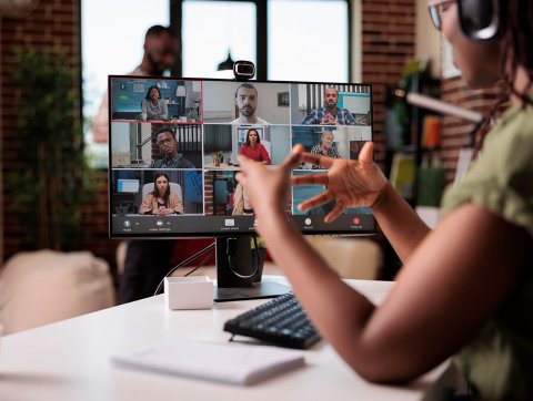A woman seated at a computer gestures with her hands as she talks to classmates online.