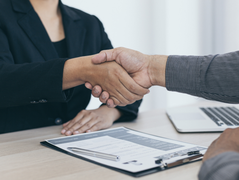 Professionals in business attire shake hands at desk