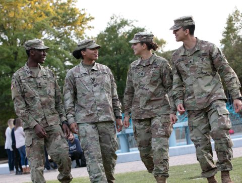 Four students in military uniform chat as they walk on campus.