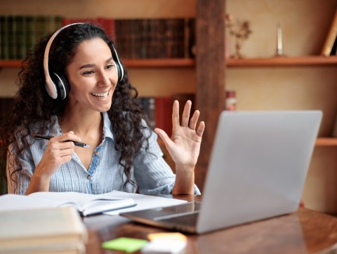 Woman sitting at desk, using computer and waving to webcam