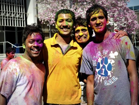 Four students covered in brightly colored powder celebrating Holi Festival.