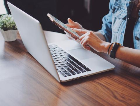 Young hipster woman using smartphone and laptop in office or