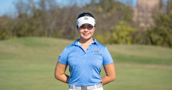 female student in a light blue polo and white visor standing on a golf course