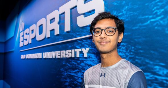 a male students stands in front of a ODU esports branded mural wall