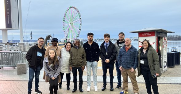 A group of students stand on a sidewalk in front of the National Harbor in Maryland. 
