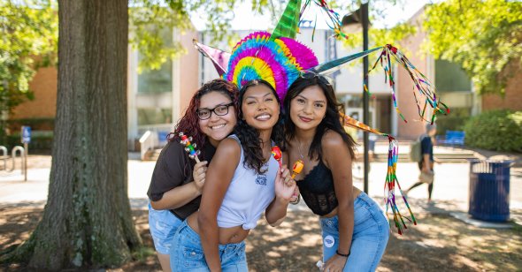 Three students stand in front of a piñata. 