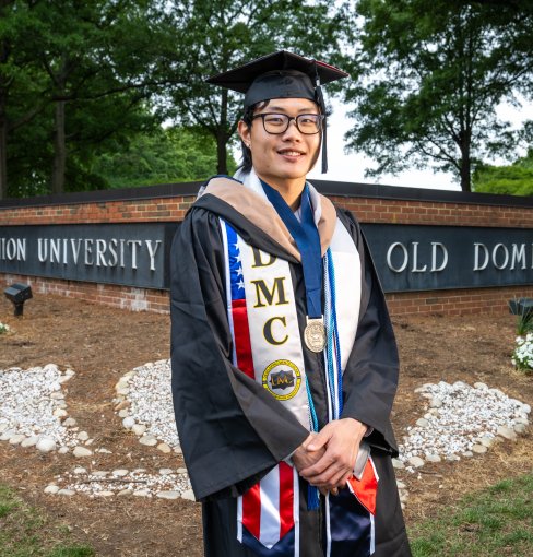 Alan Pan, 2026 ODU Honors College graduate, smiles while wearing a cap and gown in front of an ODU campus sign.