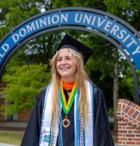 Vegas Fetterly, 2026 ODU Honors College graduate, smiles while wearing a cap and gown in front of an ODU campus sign.
