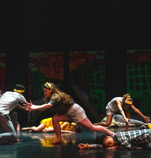 A group of students dance on a stage inside a theatre. 