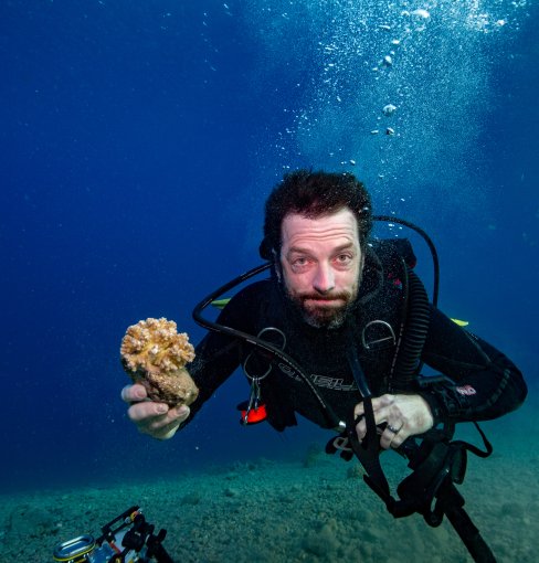 Professor Dan Barshis, Ph.D., holds a piece of coral while scuba divining. 