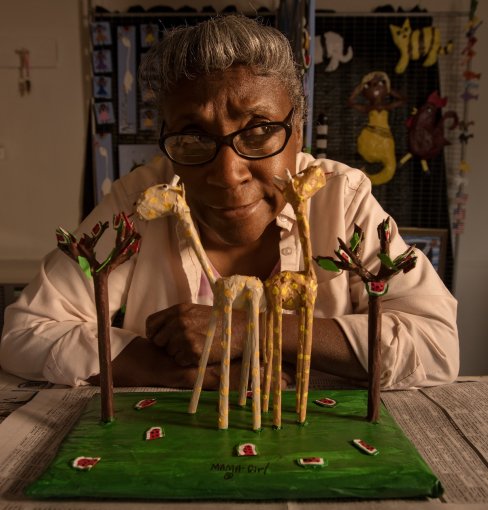 A woman sits behind a set of small animal sculptures.