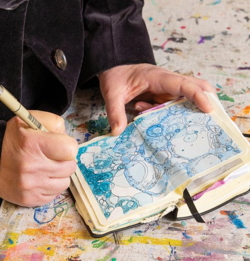 A person's hand holds a pen and draws in a small notebook 