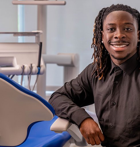 Benjamin Quansah sits next to dental chair in clinic.
