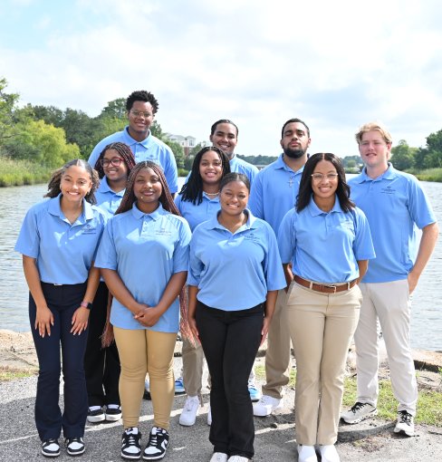 Group of students dressed in blue golf shirts standing by a pond.