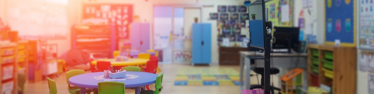 Early childhood classroom with small tables and chairs, play mats and teaching monitor.