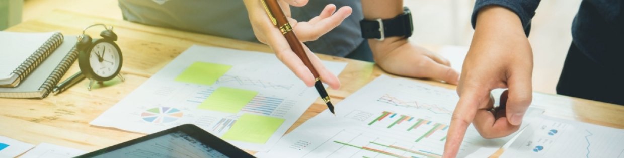 People looking over graphs and other documents spread out on a large table 