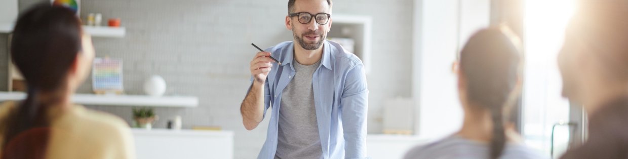 A man with thick black rimmed glasses speaking to people at a conference table. 