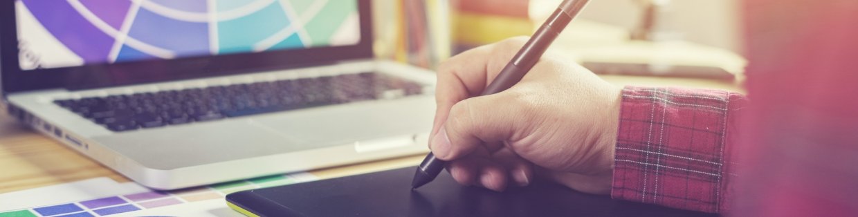 A person's hand with a pen next to a laptop with a golden haze.