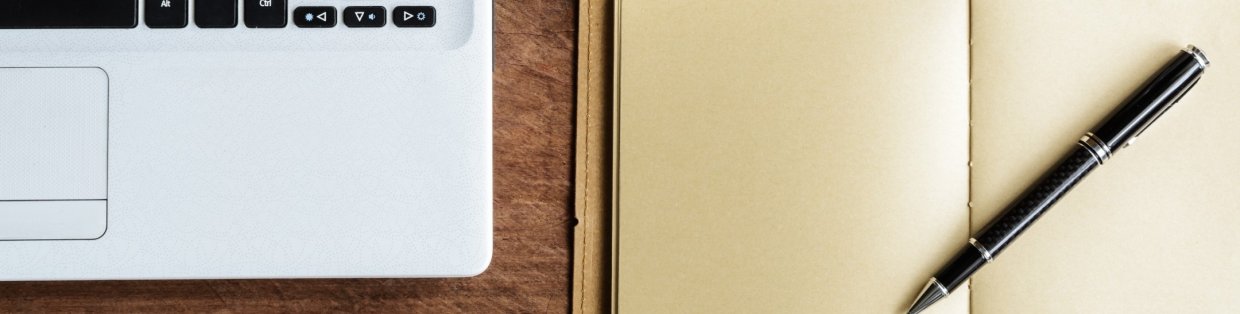 a laptop sitting next to a notebook with a pen on top.