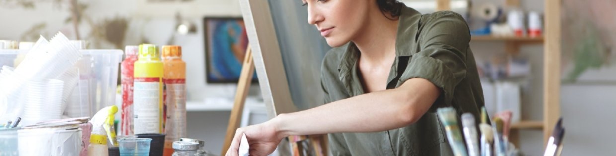 A painter mixing colors with an easel behind her.