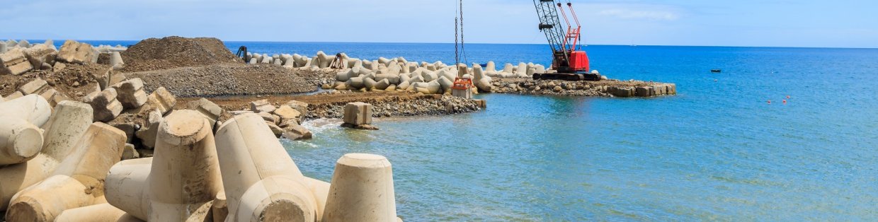 Water's edge with a crane at the end of a jetty lifting an object. 