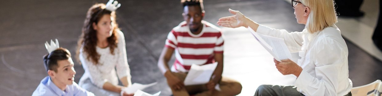A playwright speaking to her actors. Two of them wearing paper crowns on their heads while taking notes. 