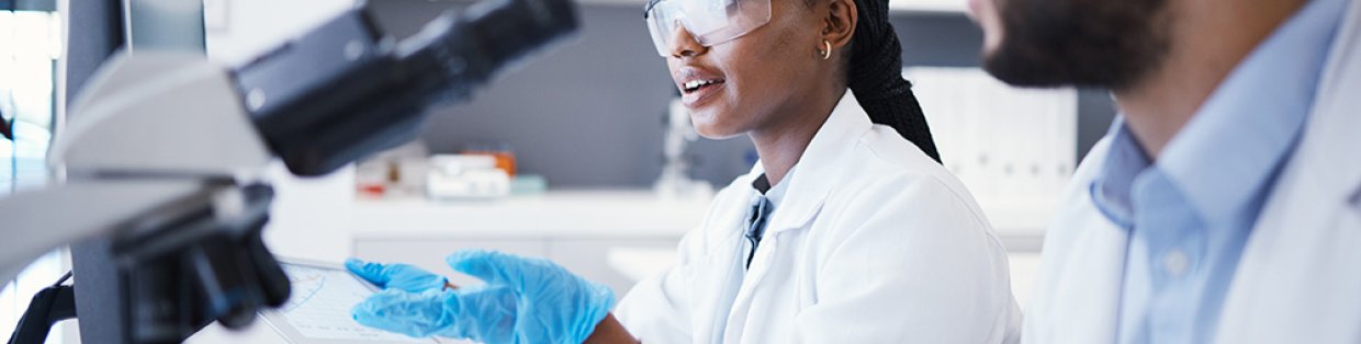 Man and woman in laboratory wearing lab coats with microscope and computers.