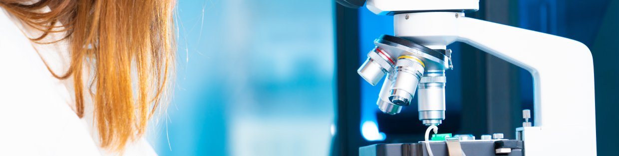 a person look through a microscope in a lab coat. 