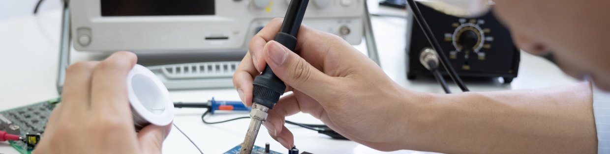 Electrical engineering banner image of student using a soldering tool on an electric panel. 
