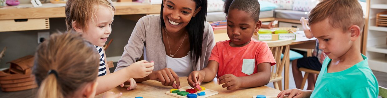 a teacher sitting in a group of young children doing arts and crafts. 