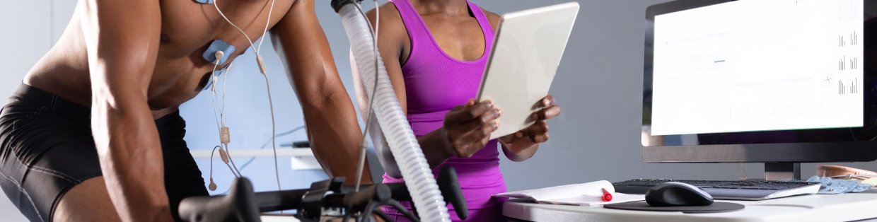 Physical education image of two people conducting a stress test. One on a bike with a mask, the other observing. 