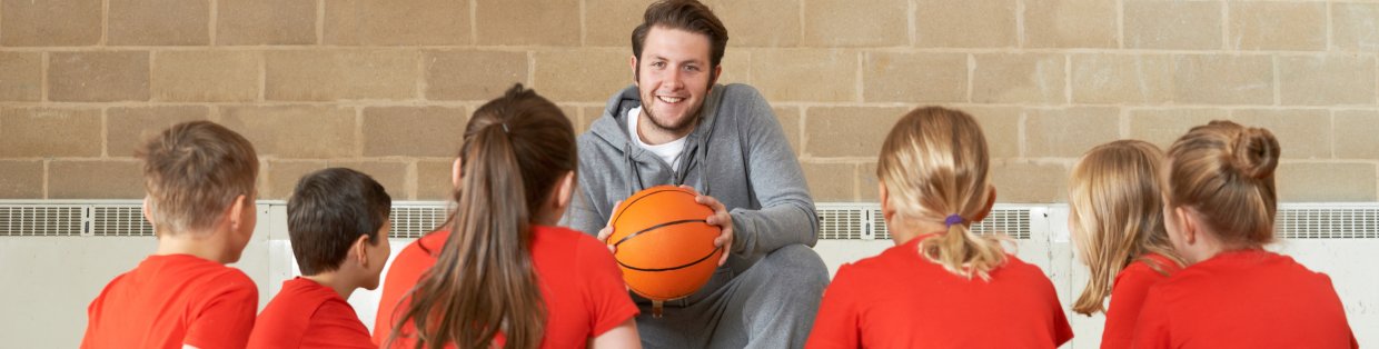 Students and coach seated on basketball court talking game plan.