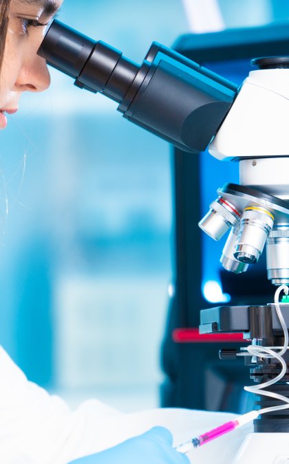 a person look through a microscope in a lab coat. 