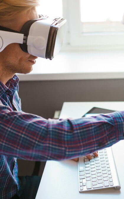 Man in VR goggles touching computer monitor