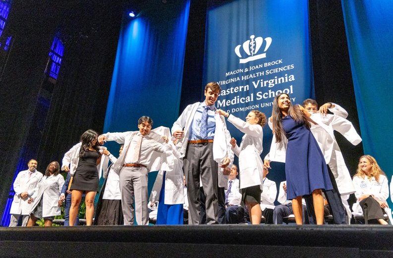 MD students on stage receiving white coats. 