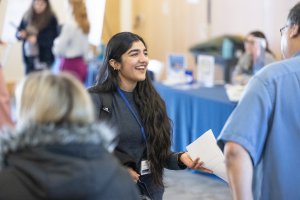 A student smiling and talking to people at an event.