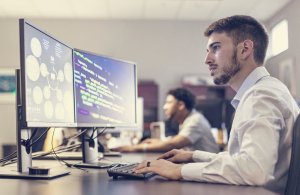 A male student is sitting at a large computer screen engaging in cyber security research
