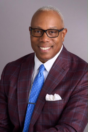 a man wearing a maroon suit, blue tie, and glasses