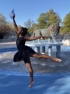 A woman strikes a dance pose in front of a fountain. 