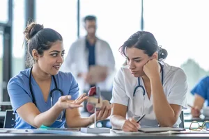 2 medical students talking in a classroom with a fake heart 