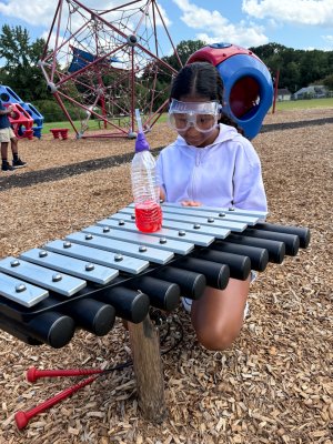 child performs an experiment with a water bottle and xylophone