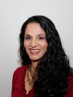 A woman with long dark hair wearing a red blouse smiles at t