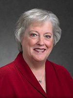 A woman with short gray hair wearing a red blouse smiles at 
