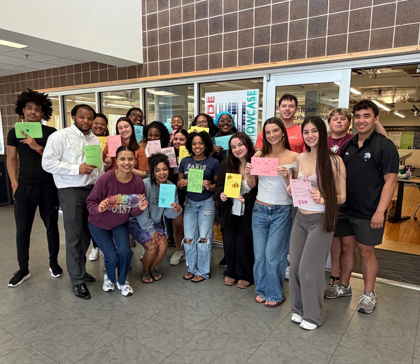 A group of students smiling at the camera holding signs with words of affirmation.