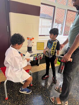 Student in white lab coat presenting botany project to another student.
