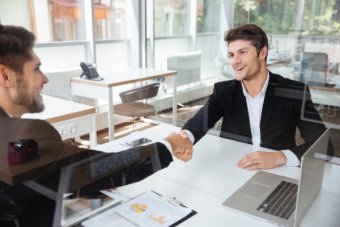 Two cheerful successful young businessmen shaking hands on b